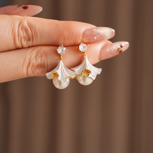 Dettaglio orecchini dorati con fiore in smalto bianco, zircone e perla tonda lucida