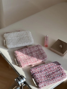 Three assorted tweed mini wallets with zipper and side labels on a beige surface