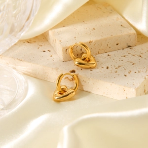 Dettaglio orecchini a cuore in oro 18K su pietra beige e sfondo di seta fluida