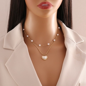 Detail of layered gold necklace featuring elegant heart pendant and white pearls on a model