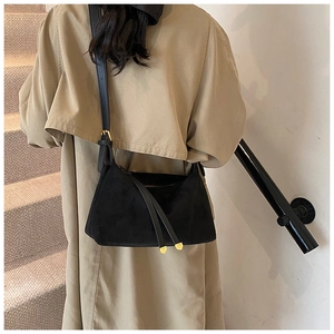 Detail of minimalist black suede shoulder bag with gold tassels worn by a model