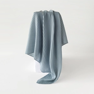 Detail of blue pleated square scarf draped over a white cube showing fabric texture