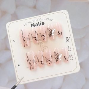 Macro view of pink glitter press-on nails with black vine patterns and 3D butterfly crystals