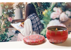 Detailed view of red soy candle in floral tin lit during a garden painting session
