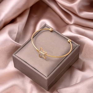 Detail of a gold-plated open star bracelet placed on a luxury silk fabric background