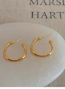 Detailed view of streamlined gold hoop earrings with irregular curves on white marble tray