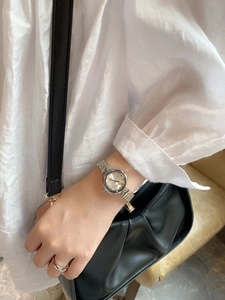 Elegant woman wearing a silver stainless steel watch with a white silk shirt and black bag