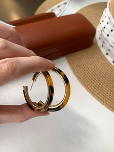 Detail of tortoiseshell resin hoop earrings with gold inner ring held by hand