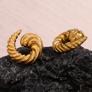 Macro detail of 18K gold plated stainless steel swirl earrings on dark stone texture