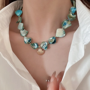 Close-up of irregular blue-green shell bead necklace with a gold seashell pendant