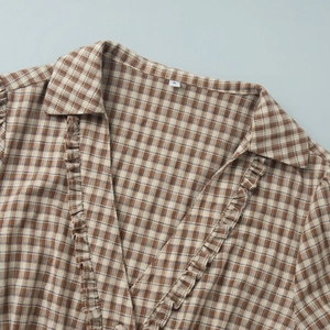 Detail of ruffled V-neck and collar on brown plaid shirt with size S tag visible