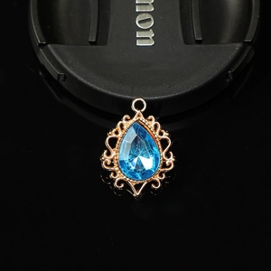 Détail macro du pendentif goutte vintage avec pierre bleue et bordure en dentelle dorée