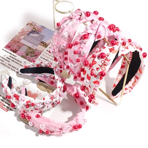 Pink and white knotted headband with imitation pearls and love letter patterns on gold stand