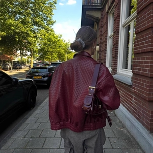 Oversized burgundy woven leather bomber jacket with a matching shoulder bag in city setting