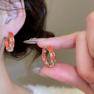 Close-up of silver needle earrings with orange and white crystals worn on model