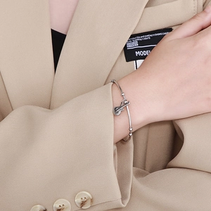 Detailed close-up of a silver violin charm bracelet on a model wearing a beige suit