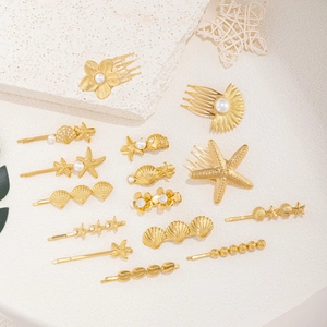 Flat lay of 12 gold hair clips with sea shells, starfish and pearls on beige texture