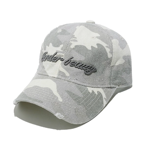 Close-up of camouflage baseball cap with Under Beauty embroidery and distressed brim