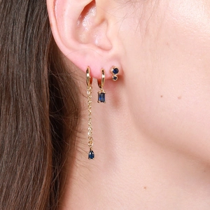 Gold earrings set with navy blue stones and long chain pendants shown on a model