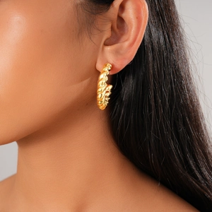 Close-up of golden twisted hoop earrings on model highlighting the woven texture