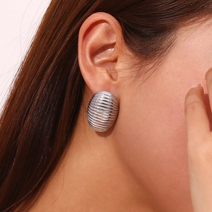 Macro view of textured silver oval stud earrings with horizontal striped pattern on ear