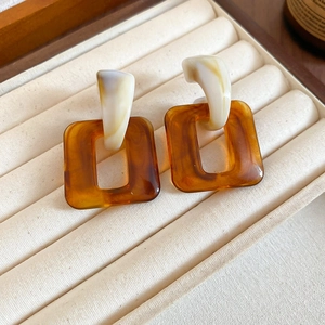 Macro detail of amber resin square earrings on beige velvet jewelry tray