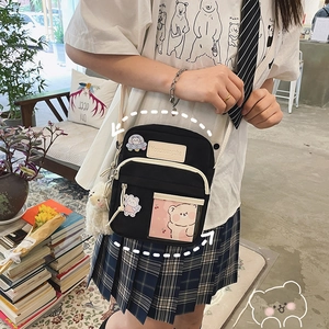 Détail du sac bandoulière noir avec poche transparente, breloque ours et écusson logo