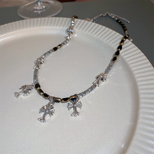 Détail d'un collier pendentif croix en argent avec perles noires sur plateau céramique