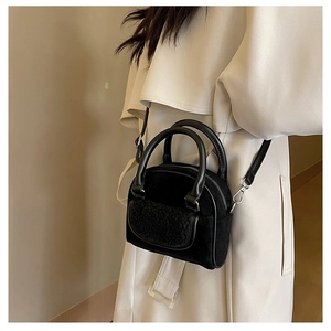 Model showcasing a small black plush crossbody bag with leather handles and beige trench coat