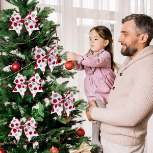 Père et fille décorant le sapin de Noël avec des nœuds à paillettes dans un salon cosy