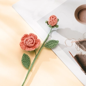 Detailed handmade crochet rose in peach pink yarn on a warm creative desk setting