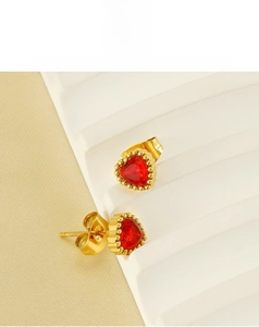Detail of gold-plated heart earrings with red zircon center on white display stands
