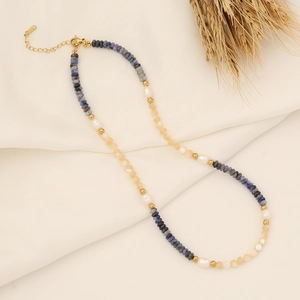 Dettaglio della collana in pietre naturali e perle su tessuto bianco con decoro di grano