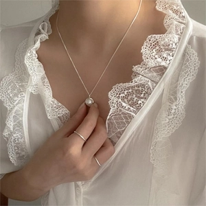 Detail of elegant freshwater pearl necklace and minimalist silver rings on a model