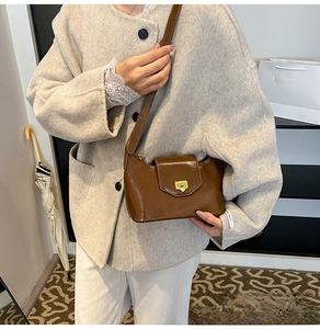 Brown retro crescent shoulder bag in glossy leather with magnetic buckle on gray coat