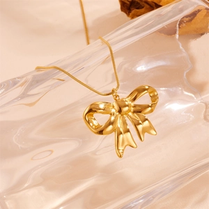 Elegant gold bow pendant necklace on a sleek snake chain displayed on a glass vase