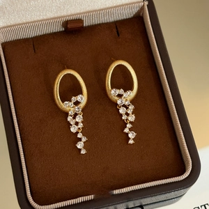 Gros plan de boucles d'oreilles dorées à pompons et cristaux dans un écrin en velours