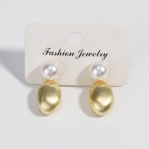 Detail view of pearl stud earrings with brushed gold oval metal charms on display card
