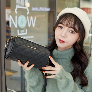 Elegant black quilted cylindrical crossbody bag with gold logo on green sweater model