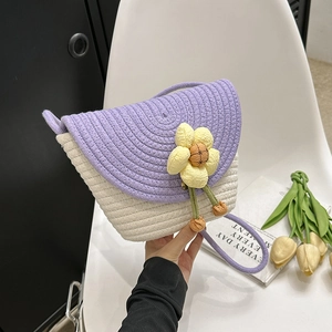 Detail of handmade woven straw bucket bag with floral charm and purple shoulder strap