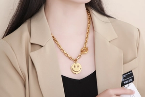 Close-up of gold chunky chain necklace featuring a smiley pendant and T-bar clasp