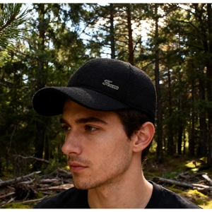 Detail of a black winter baseball cap with ear flaps and Jeans metal tag in the forest