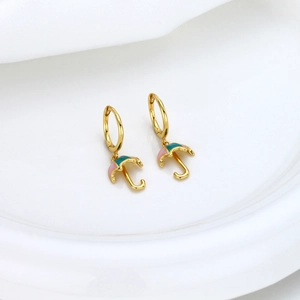 Detailed macro of gold umbrella earrings with green and pink enamel on a white surface