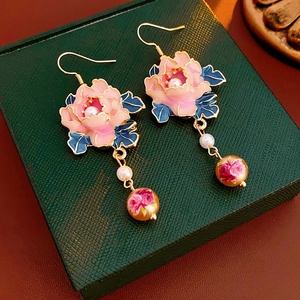 Detailed view of pink flower earrings with pearls and floral beads on green box