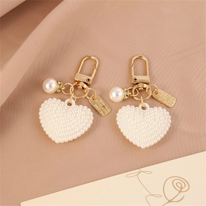Golden heart pearl keychain with rhinestone ring and rectangular pendant on pink fabric