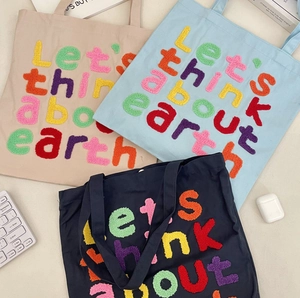 Detail of three canvas tote bags with colorful chenille embroidery letters on light desk
