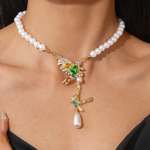 Detailed close-up of pearl necklace featuring golden bird pendants with vibrant gemstones