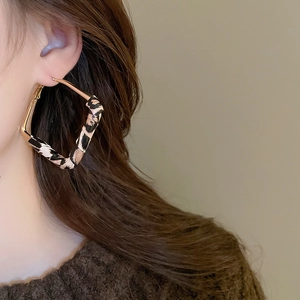 Detail view of geometric gold diamond earrings featuring leopard print fabric on model