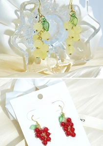 Detail of red and yellow grape earrings featuring green leaves and elegant golden hooks