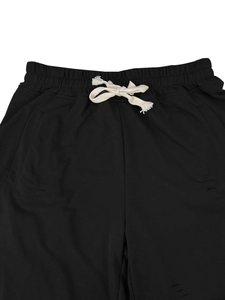 Detail view of black drawstring shorts featuring white cord and distressed torn fabric texture